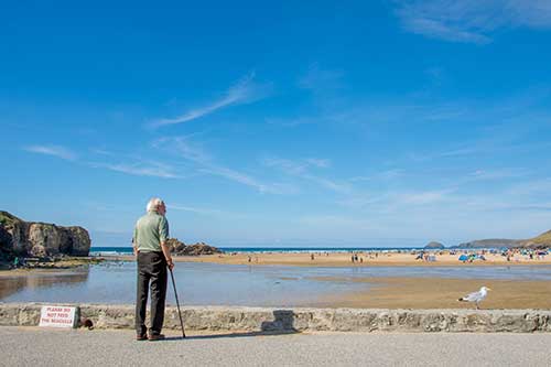 En man med käpp står vid stranden